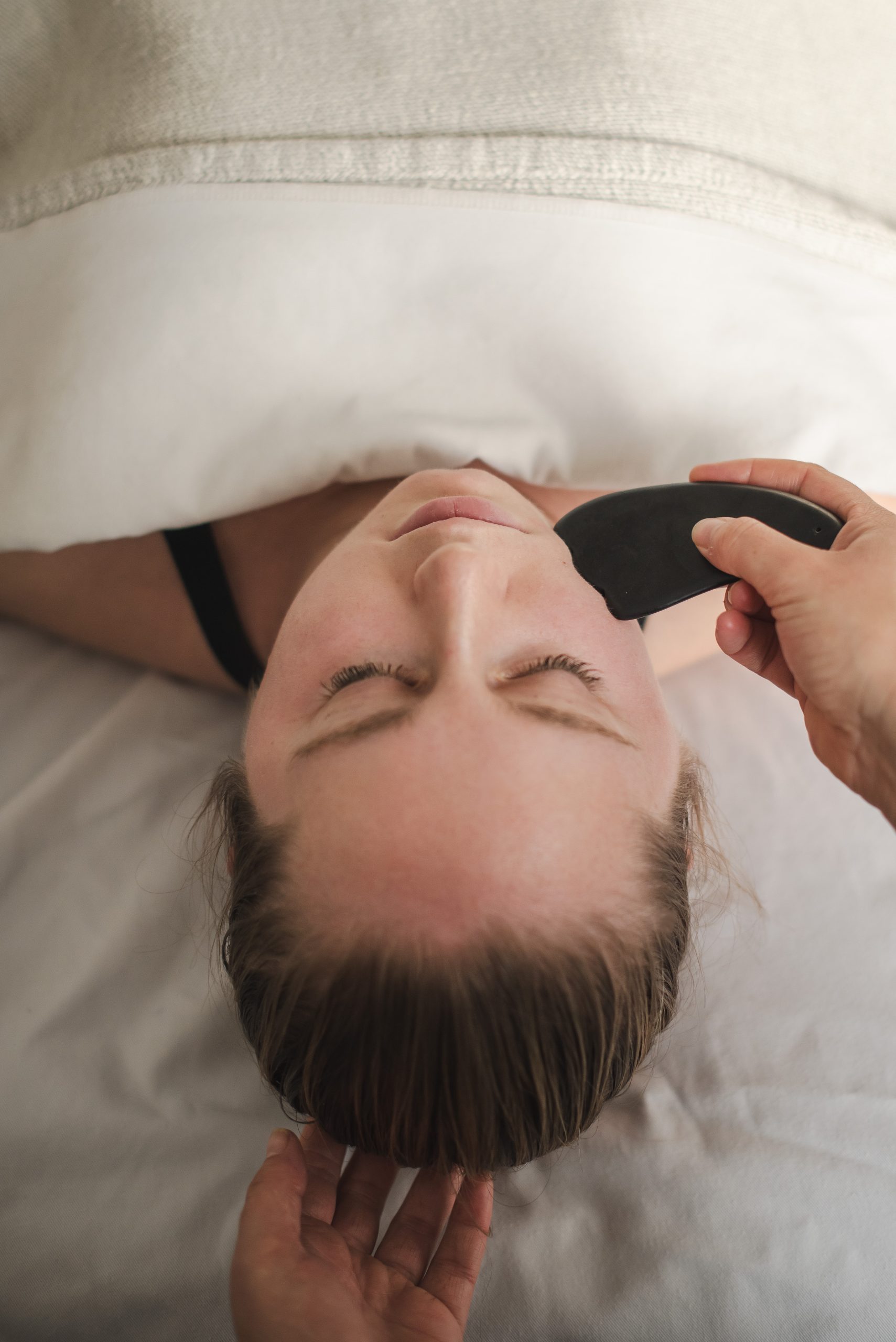 A woman receives guasha treatment for TMJ on her jaw.